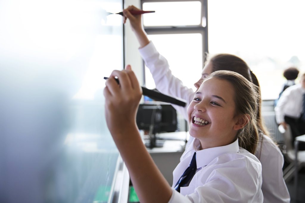 Two children in school uniform writing on a whiteboard