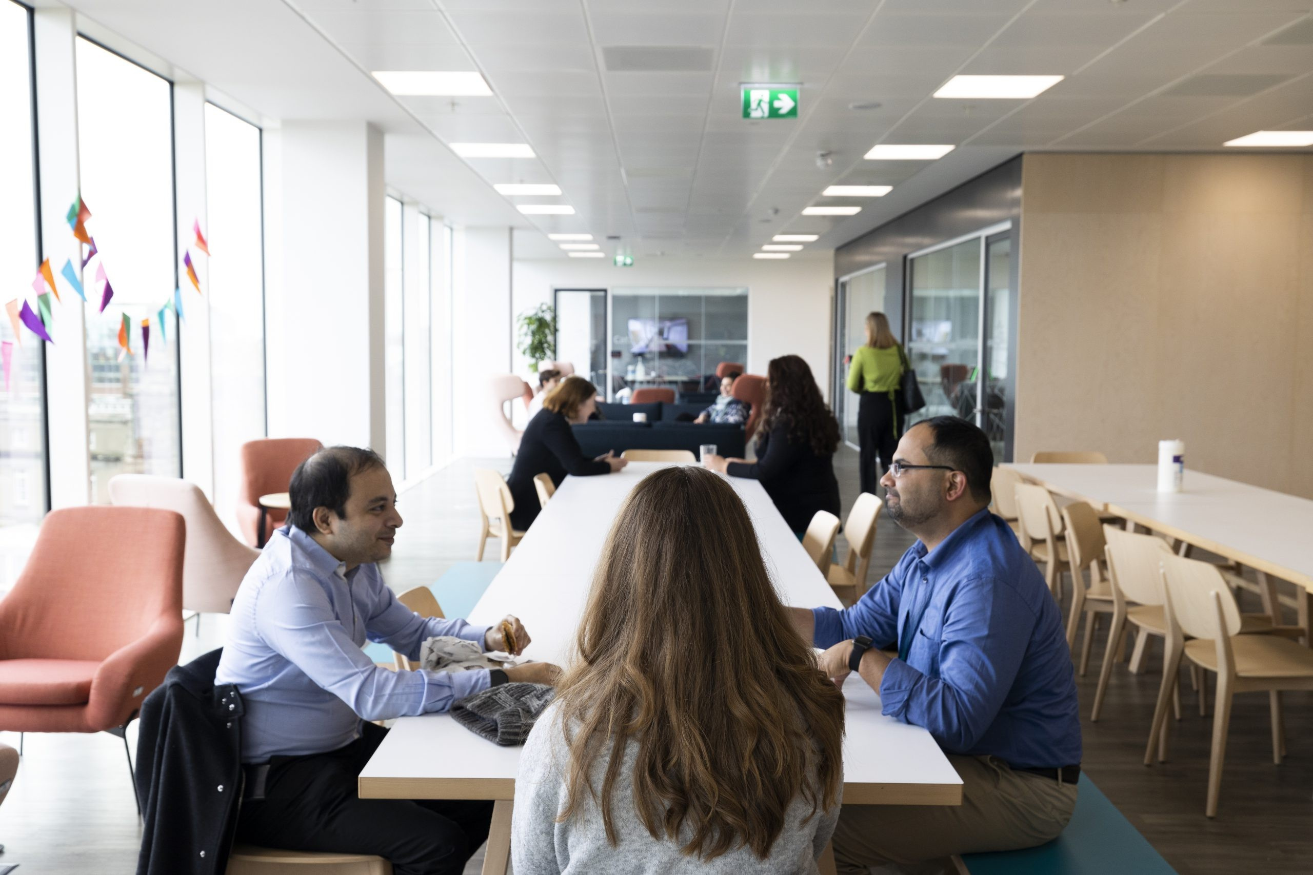 Group of people sitting at a table talking in an office social space. 