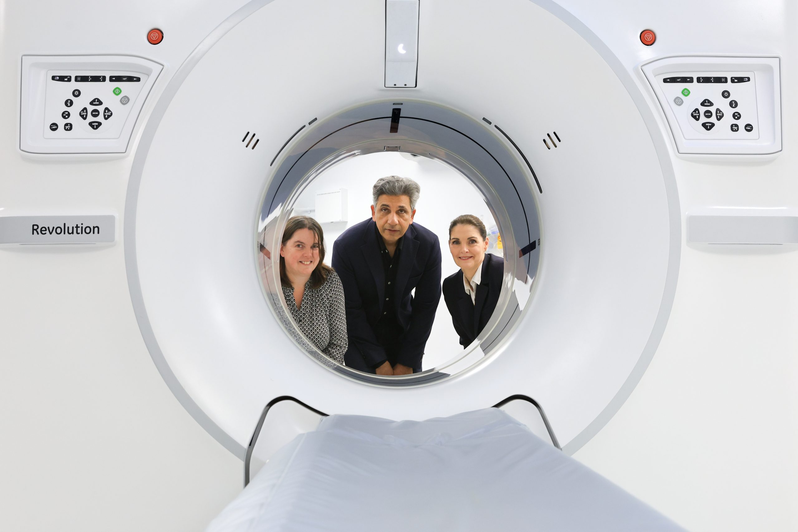 Three people looking through a CT scanner