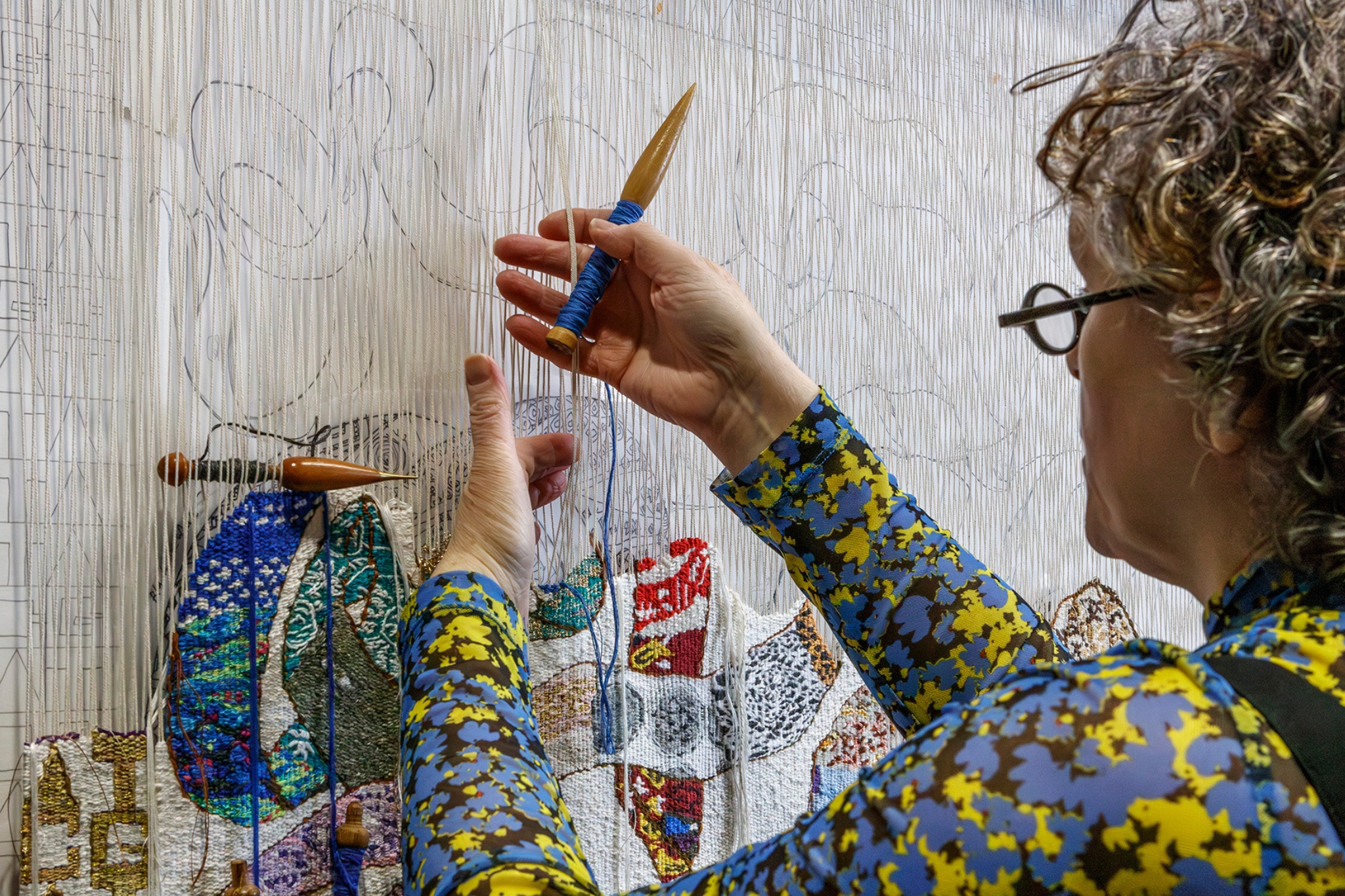 A picture of Lorna Donlon working on a tapestry|A picture of Lorna Donlon, working on a tapestry.