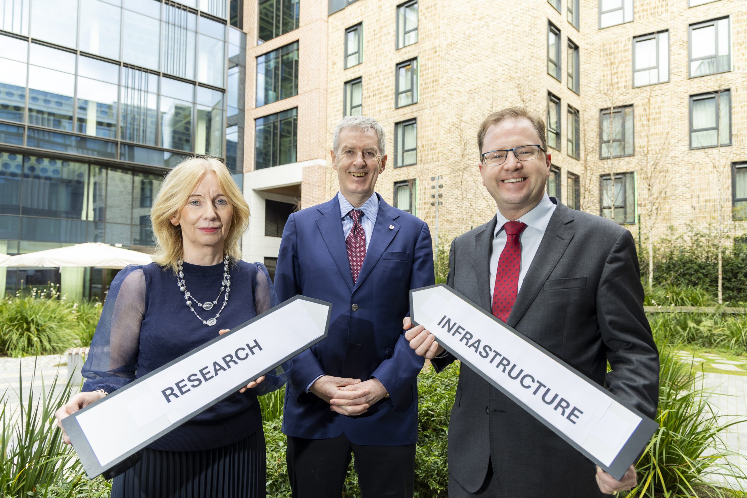 A picture of, named from left to right, Left-right: Interim CEO of Research Ireland, Celine Fitzgerald, Research Infrastructure awardee, Prof. James Meaney of Trinity College Dublin, and Minister for Further and Higher Education, Research, Innovation and Science, James Lawless TD. Celine Fitzgerald is holding a sign that says 'Research' and Minister Lawless is holding a sign that says 'infrastructure.'.