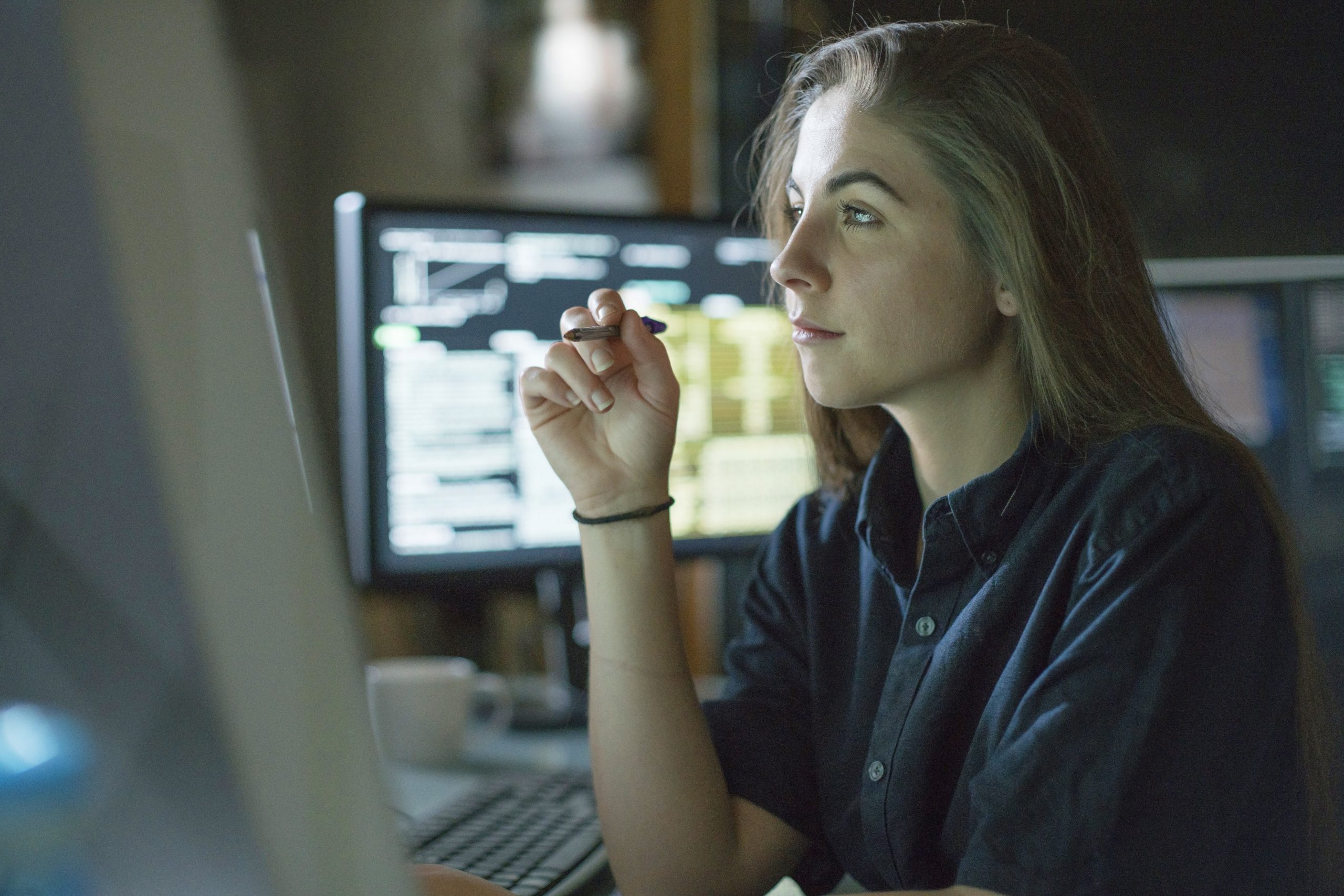 |This image shows four people talking around a table|a person holding a pen sitting at a desk. In the background there is a computer screen.