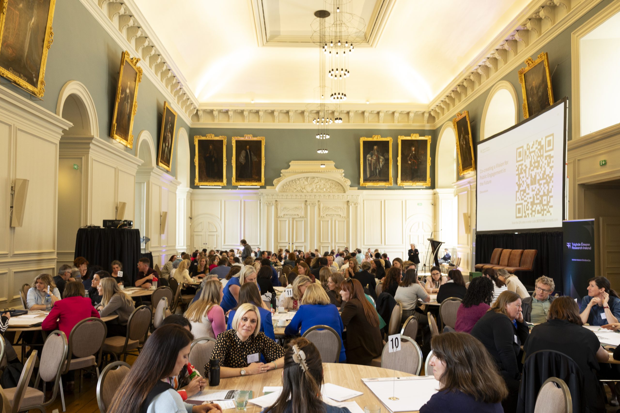 Image shows people sitting at round tables at Consensus Conference